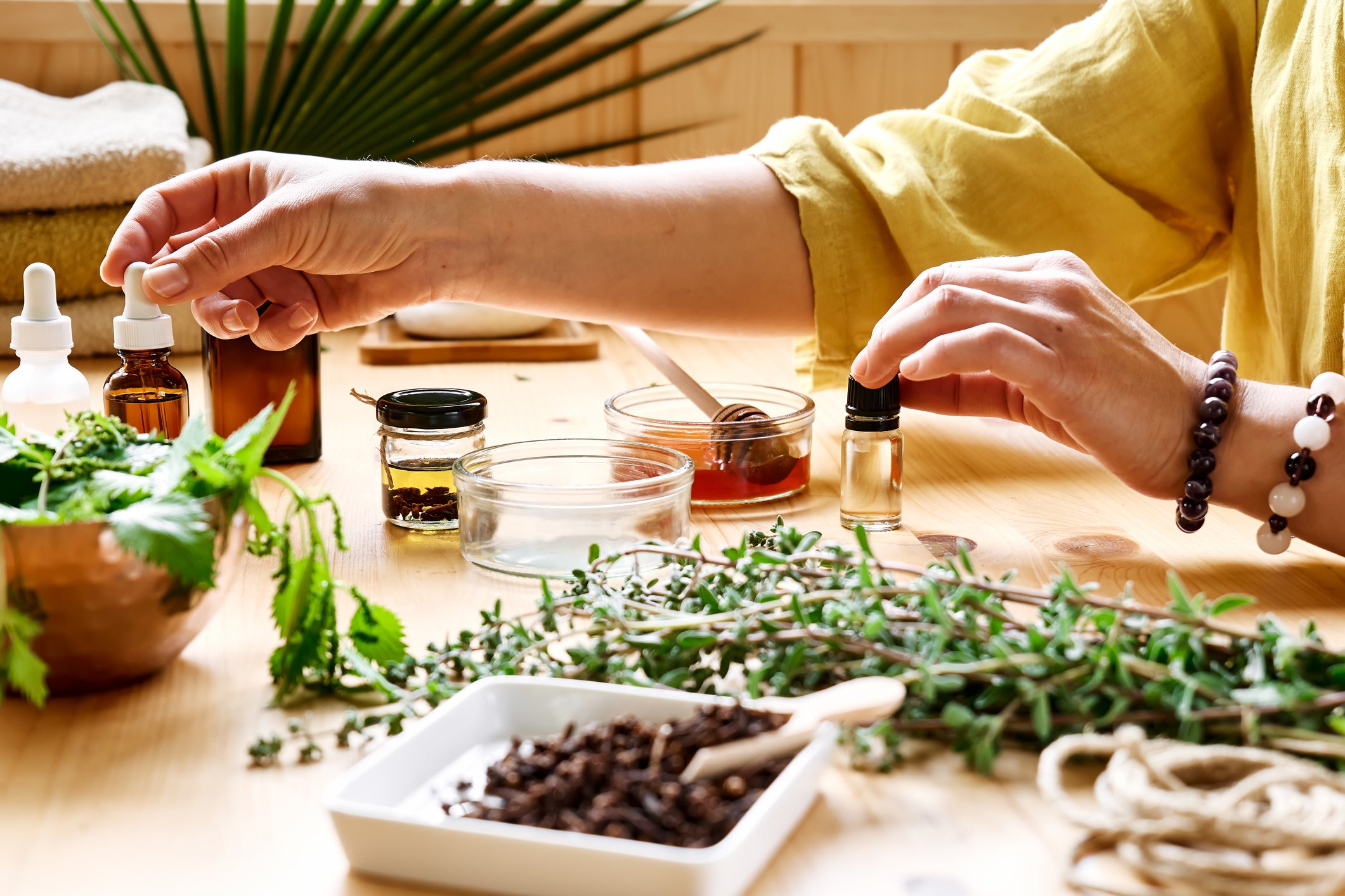 A lady concocting herbal remedies on a table with various herbs, droppers and other natural ingredients.