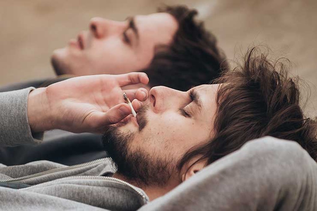 Two men laying down and smoking a joint