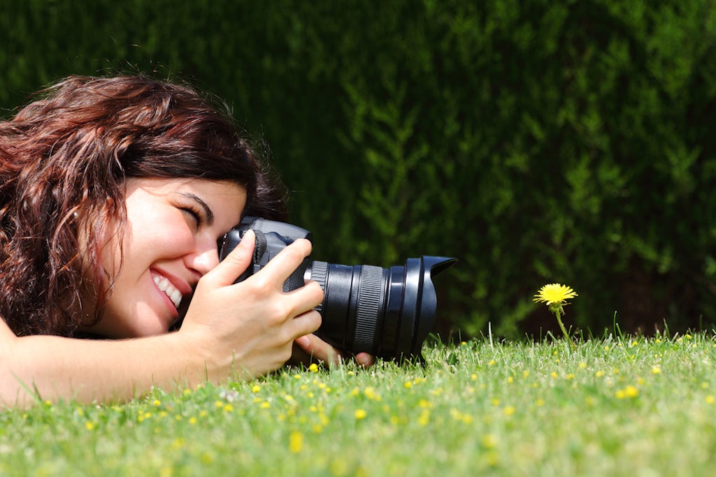 A woman takes a macro photograph of a flower in the park