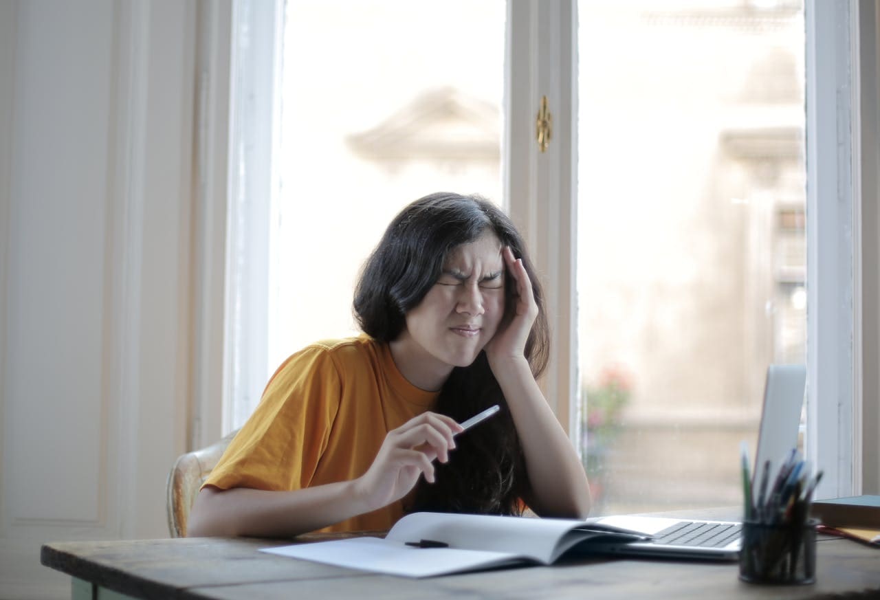 A girl sitting while holding her head as she suffers with migraine
