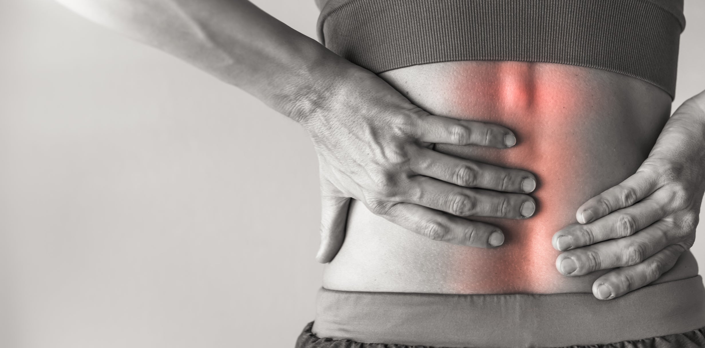 A lady suffering from lower back pain, using their hands to support their lower back.