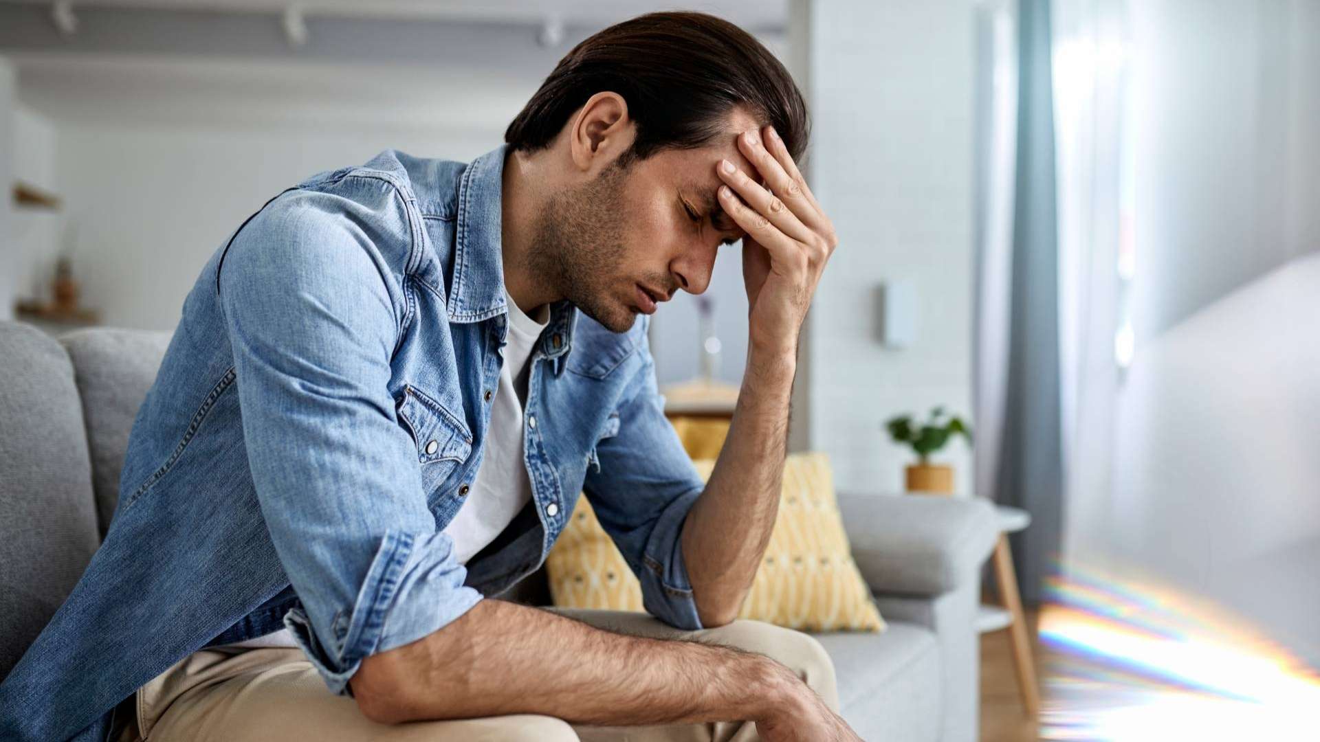 A man on a couch with his head in his hands, reflecting on stress and the potential benefits of cannabis for relief