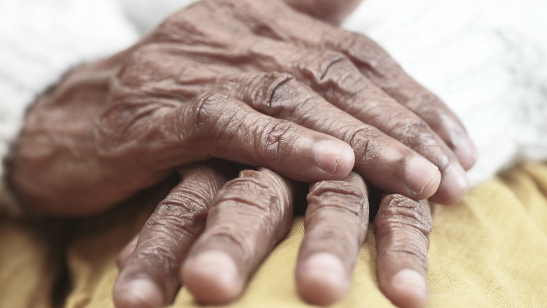 An elderly woman's hands resting on a bed, symbolizing the impact of cannabinoid medication for rheumatoid arthritis