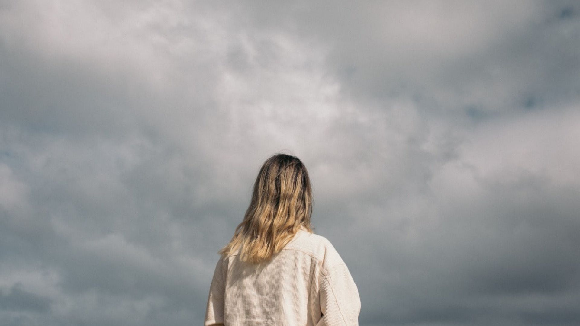 A woman stands on a beach, gazing at the sky, reflecting on themes of cannabis for mental health and depression