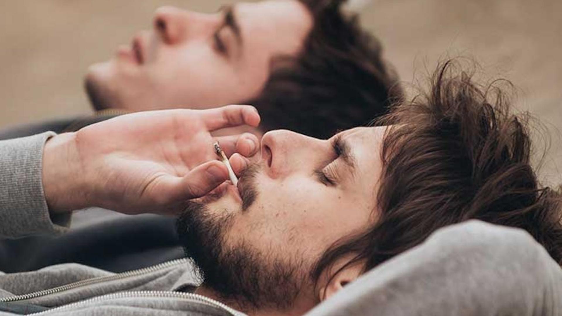 Two men on the ground smoking a joint, depicting a moment of relaxation for cannabis use for stress relief.