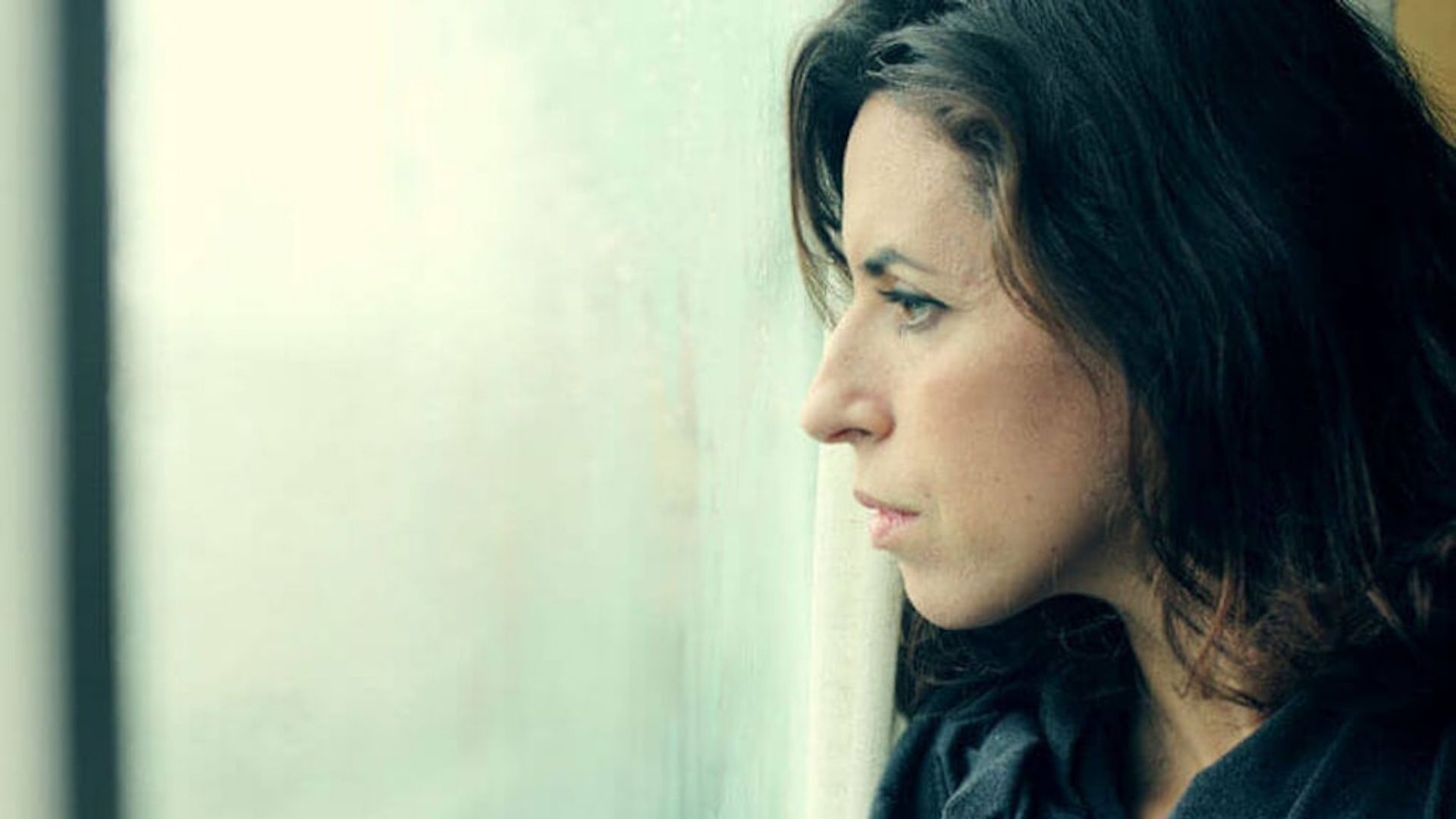 A woman gazes, looking anxious, out a window, reflecting on the use of cannabis for managing anxiety
