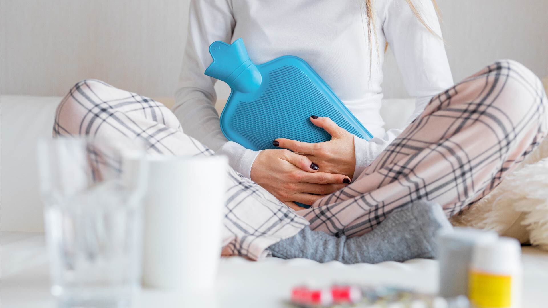 A woman sitting with her legs crossed holding a heat pad, suffering from period cramps