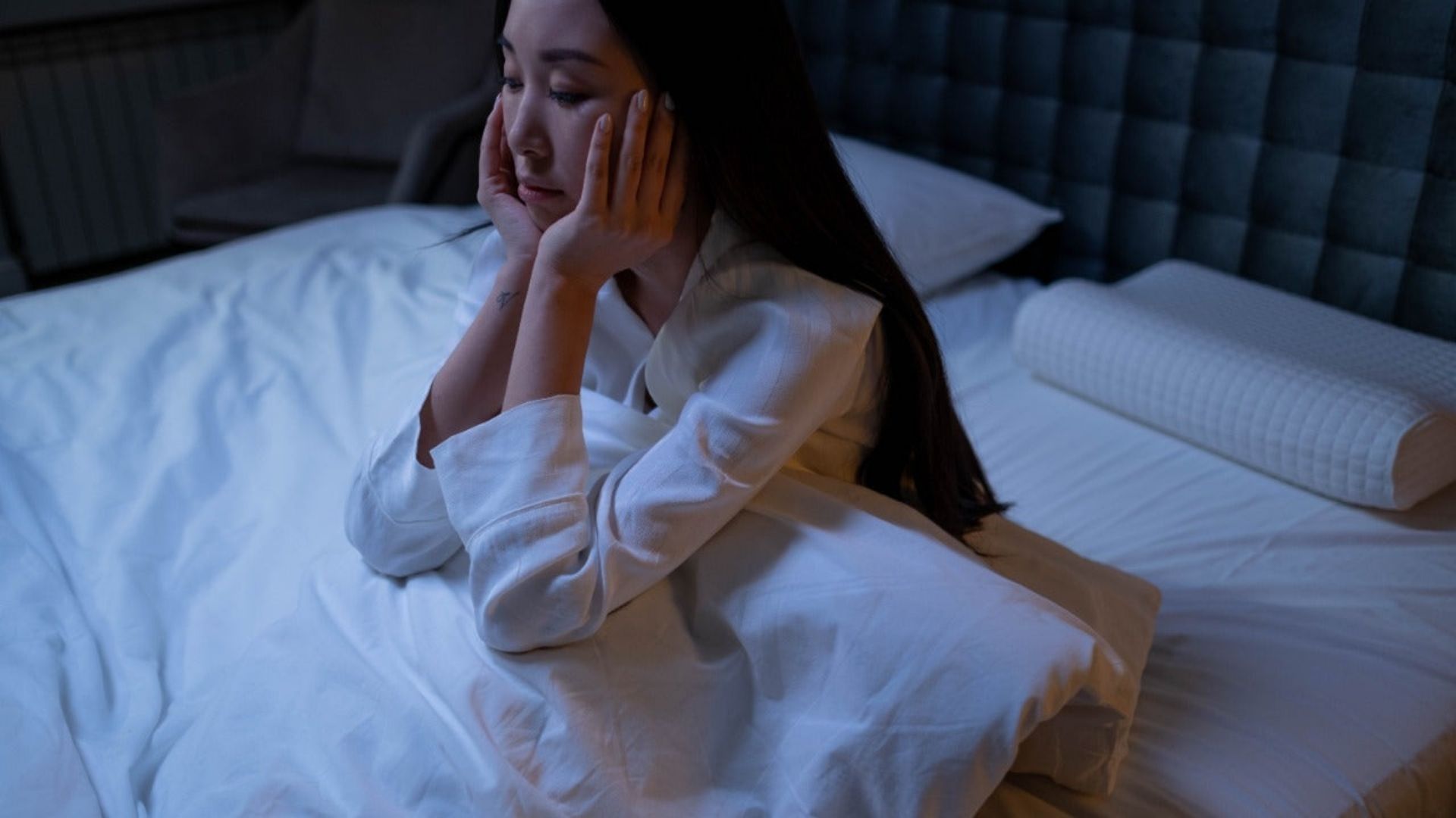 A woman seated in bed, hands on her face, considering how cannabis may help with insomnia relief