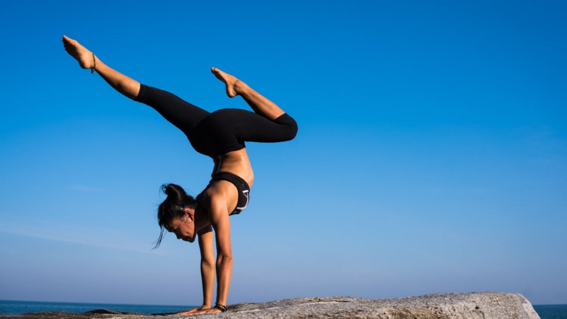 A woman balances in a handstand on a rock, representing vitality and wellness in alternative health regimes